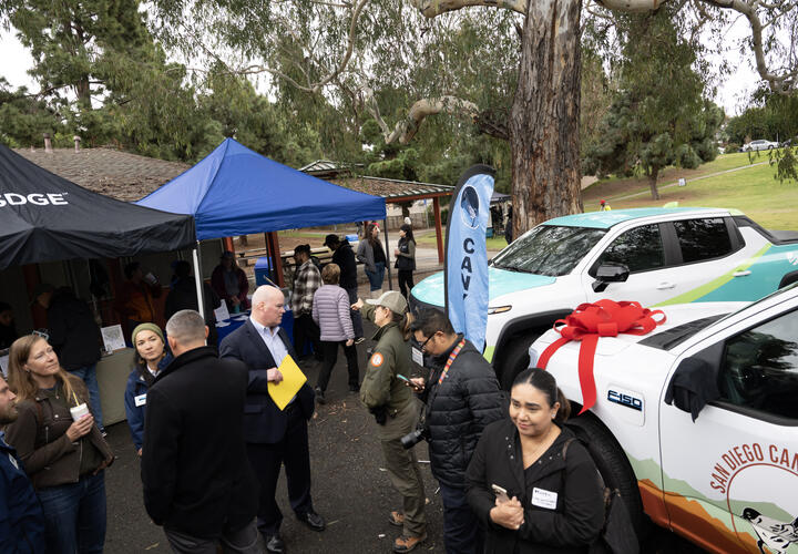 A wide shot of the event with attendees mingling with two of the donated electric vehicles in the backdrop