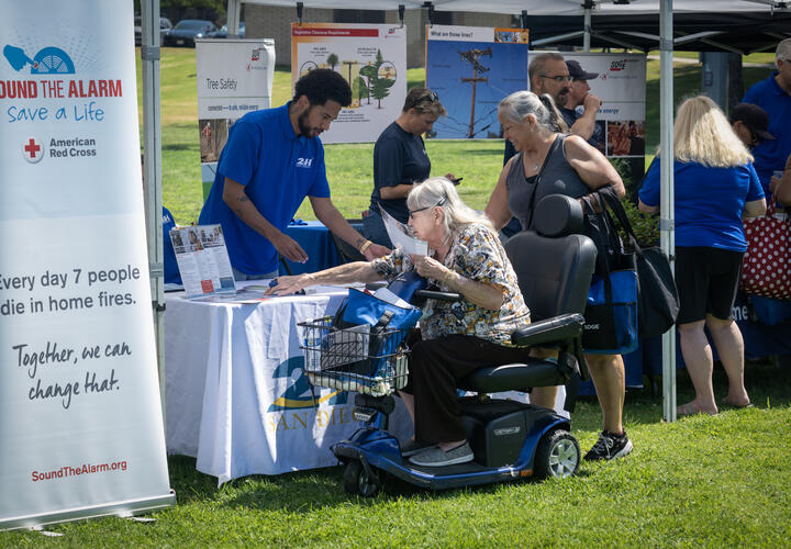 A woman driving an electric scooter, stops by a tent hosted by 211 San Diego.
