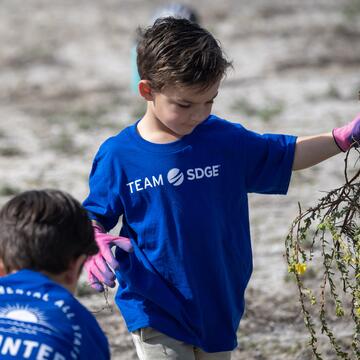 A young boy holding vegetation waste during a volunteer event at mission bay San Diego.