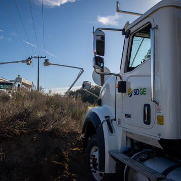An SDG&E truck in the foreground and field crews operating equipment in the background.