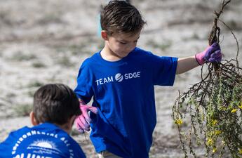A young boy holding vegetation waste during a volunteer event at mission bay San Diego.
