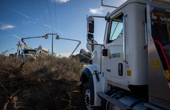 An SDG&E truck in the foreground and field crews operating equipment in the background.