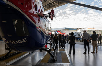An image that shows the back of a helicopter with an SDG&E logo and a press conference taking place in the background.