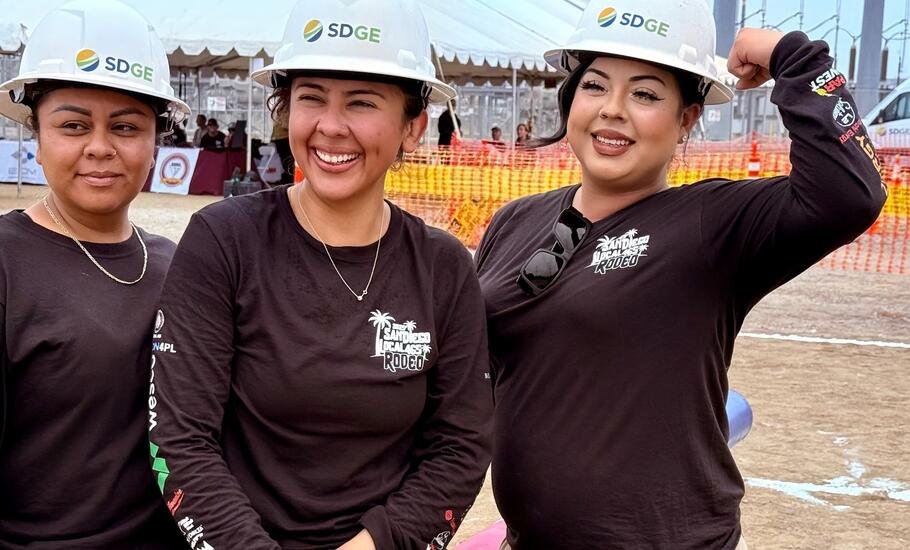 Three smiling women wearing white SDG&E hard hats pose for a photo.