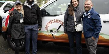 Event attendees pose for a photo with two donated electric vehicles in the background