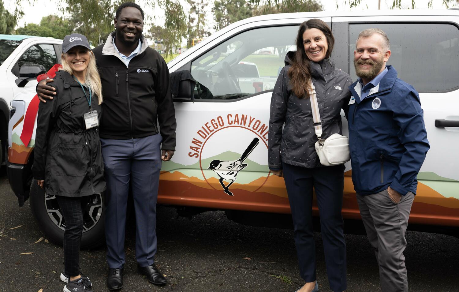 Event attendees pose for a photo with two donated electric vehicles in the background