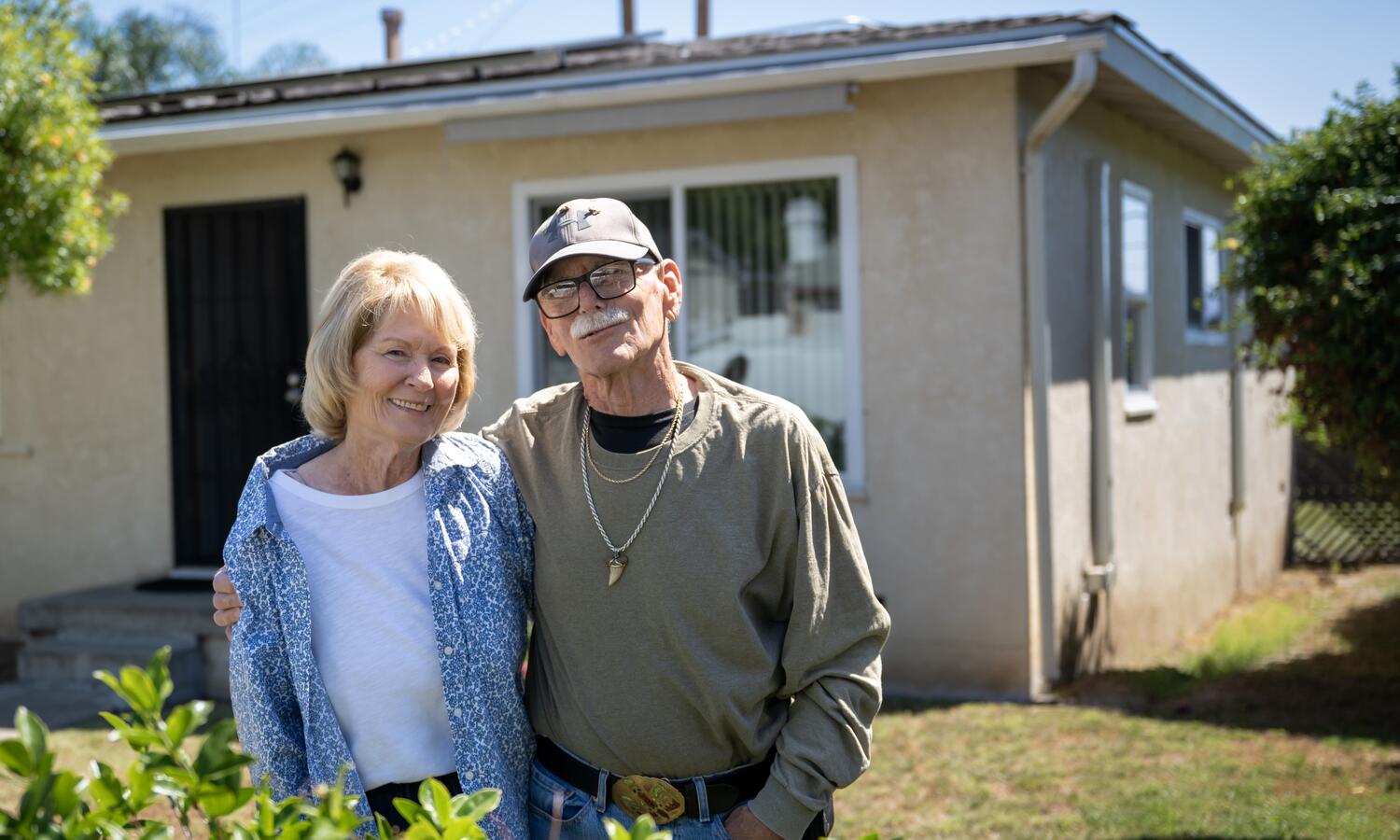 A man and women pose for a photo outside their home.