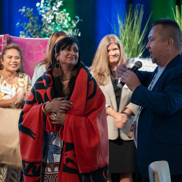 A man holding a mic at the Tribal summit, interacting with a woman wearing a red shawl.