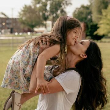A woman holding her small child in a scenic, park-like setting. 