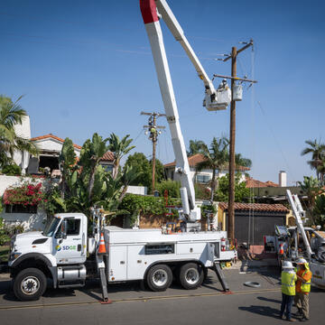 A photo of an SDG&E utility vehicle with a frontline utility worker making a repair to a power line. 