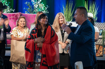 A man holding a mic at the Tribal summit, interacting with a woman wearing a red shawl.