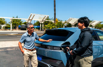 Two men talk as the younger of the two charges his electric vehicle.