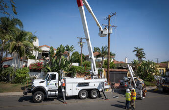 A photo of an SDG&E utility vehicle with a frontline utility worker making a repair to a power line. 